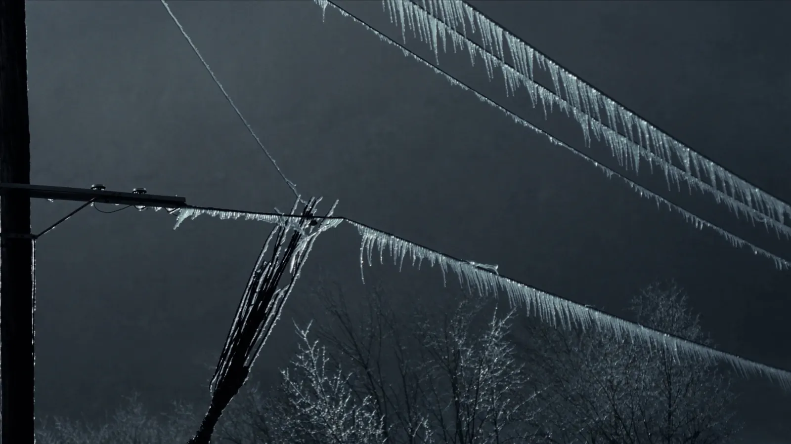Ice-coated power lines and a wooden hydro pole under a heavy grey sky
